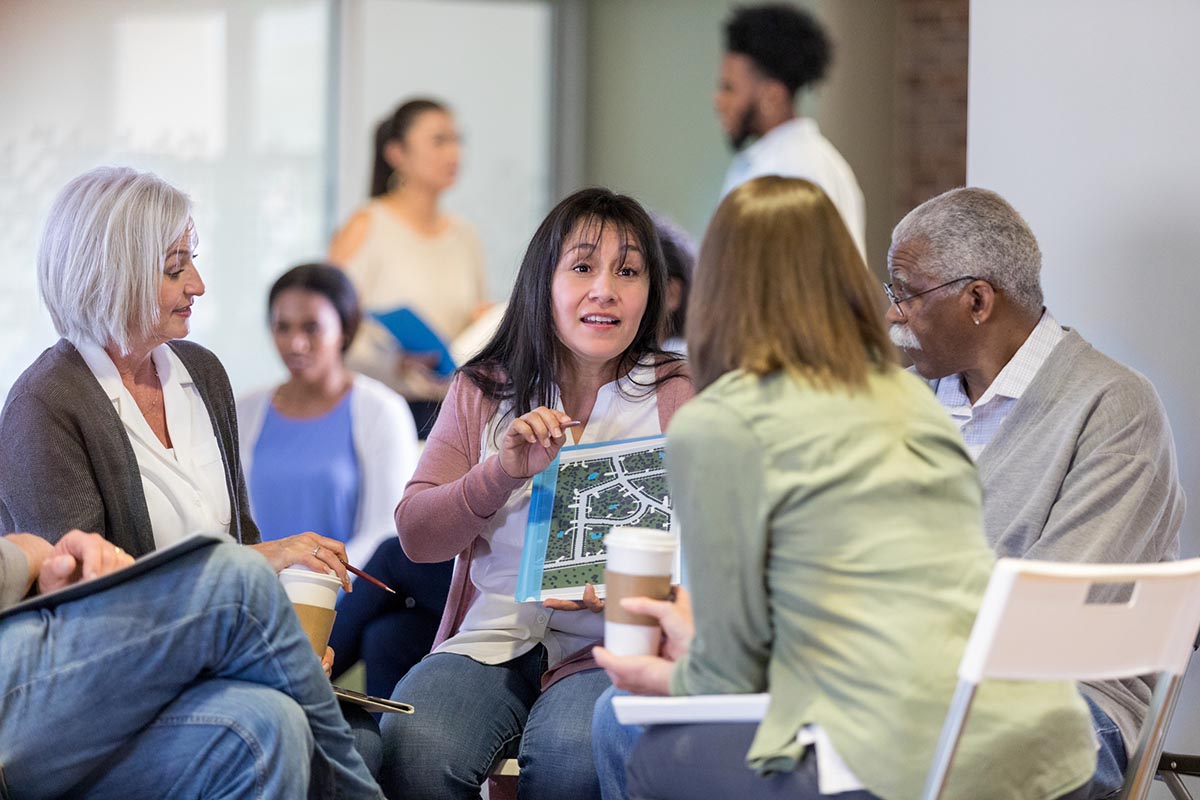 A community association manager leads a discussion with homeowners, showcasing a neighborhood layout plan. Is a CAM license worth it for managing associations?