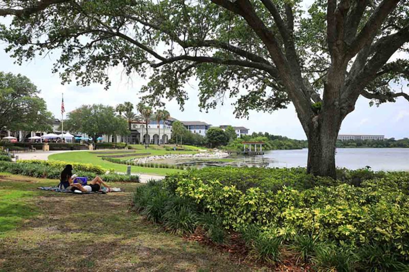 Baldwin Park, Orlando, USA - May 18, 2024: Girls reading and relaxing under a large shade tree by Harbor Park.