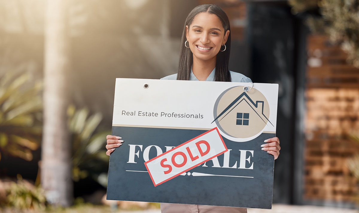 woman holds for sale sign in front of home - how much do real estate agents make in Orlando